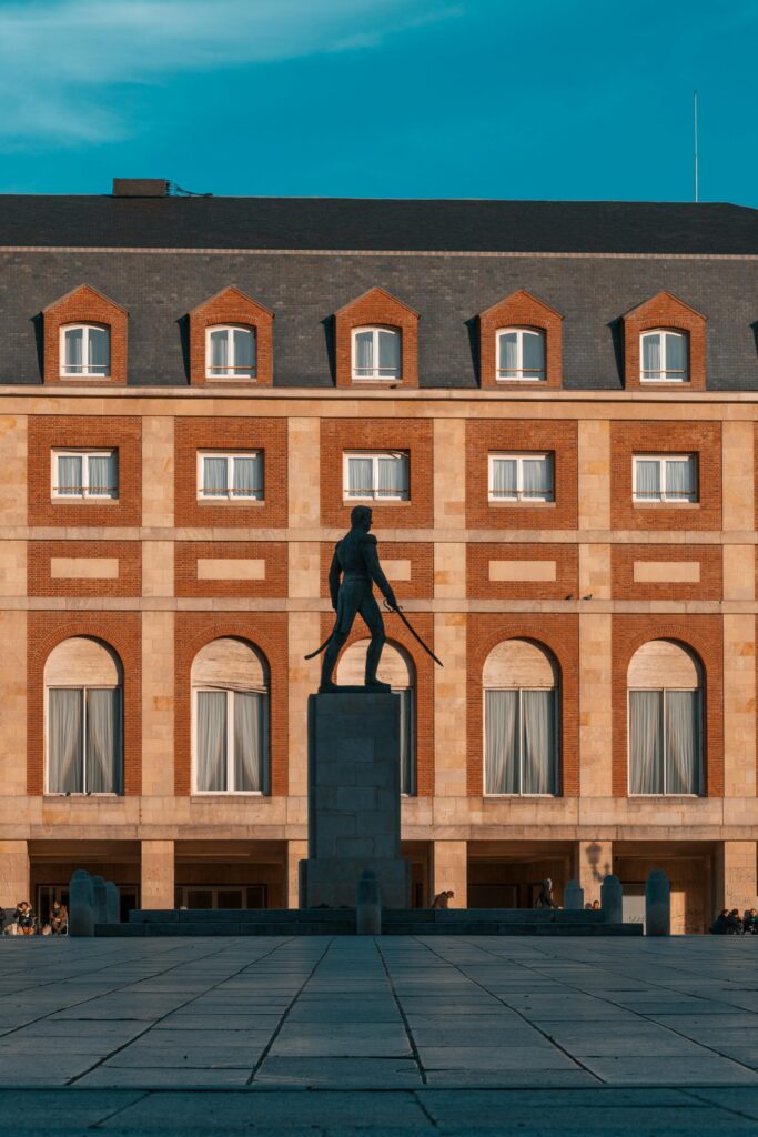 Dramatic silhouette of a statue with a historic building backdrop in Mar del Plata, Argentina.